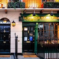 An exterior picture of 221B Baker street with a black door and the windows of the museum next to it.