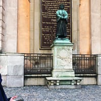 A woman in a blue coat is looking up at a bronze statue of a man