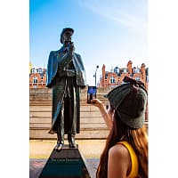 A young woman in a deerstalker hat is taking a picture of a Sherlock Holmes statue