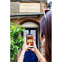 A woman is holding up her smartphone against a brick facade with a signs that says Sarsden building
