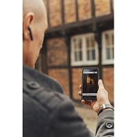 A man standing in front of a half timbred house is holding up his smartphone