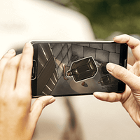 A woman's hands are holding a smartphone. On the screen is an image of old items strewn about in a prison cell.