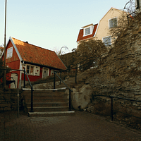 A small red wooden house with a stone staircase leading up beside it.