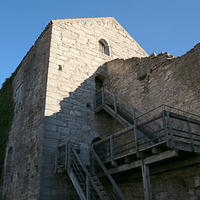 A photograph of the Kajsarn prison tower against a very blue sky. There is a wooden staircase leading up the side of the tower.