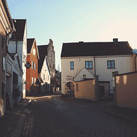 A photo of Strandgatan in Visby. There is a cobblestone street with low white, pink and yellow stone buildings lining it.