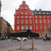 A metal monument displayed in an open space. in the background is a big, red stone building