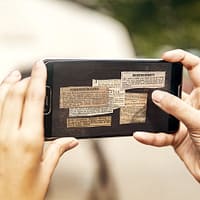 A closeup of a mobile phone screen. on screen are several old newspaper articles visible