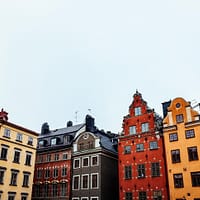 A collection of medieval stone houses in various bright colors are clustered under a grey sky