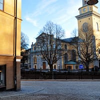 A sunset view of the Maria Magdalena church in Stockholm. It is a yellow stone building with a large belltower with green details.