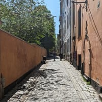 A narrow alley in Stockholm old town. The alley is paved with cobblestones and the buildings on either side are a pale yellow.
