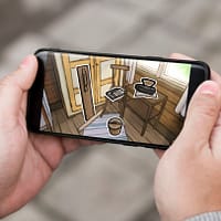 Two hands are holding a smart phone. On the screen is an illustration of the interior of a small cabin in the early 1900's.