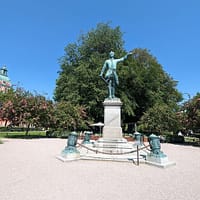 an open space in the King's garden park in Stockholm. The is a large copper statue in the middle, and trees and flowers on the side.