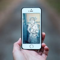 A hand is holding a smartphone. On the screen is the image of a viking ghost wearing a helmet.