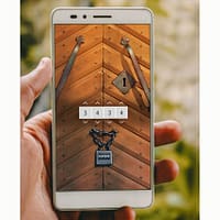 A closeup of a hand holding a smartphone. On the screen is a puzzle where you are supposed to crack a code the lock hanging on a church door.