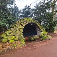 A photo of a small, man-made cave covered in green moss.