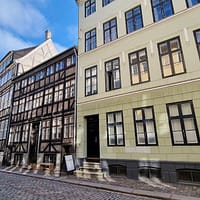 A photo of a street in central Copenhagen, with a half-timbered building in the foreground, against a clear blue sky.