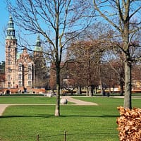 A photo of the Kongens have park in Copenhagen. Green grass lawns and bare trees against a clear blue sky.