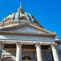 A zoomed in photograph of the Marble church tower in Copenhagen. The sky is clear blue and the dome of the church is clad in green copper.