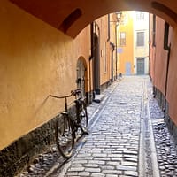 A photo of a covered alleyway in Stockholm's Old town. The surrounding buildings are dark yellow, and an old bike is leaning against a wall.