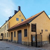 A photograph of the Kronhusbodarna market area in Gothenburg. It consists of a series of low, yellow stone buildings around a cobble stone square.