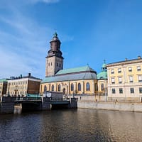 A photograph of one of the many canals in Gothenburg. A bridge is running across the water and on the other side is a large stone church with a green copper roof.