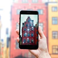 A close up photo of hands holding a smartphone. On the screen is an image of a haunted building, with skulls floating around in the air.