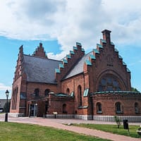 Ett foto av St Nicolai kyrka i Trelleborg. Kyrkan är i rött tegel, med trappgavlar. det är en fin sommardag med blå himmel och stackmoln.