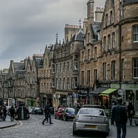 A photo of Cockburn street in Edinburgh on a grey day. People are rushing across a busy street.