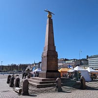 A photo of the obelisk statue at Kauppatori square in Helsinki on a day with clear blue sky.