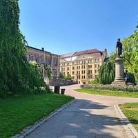 A photo of the University park in Uppsala on a sunny day. yo ucan see the Carolina library in the background.