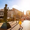 A young woman in a yellow dress is standing in front of the Sherlock Holmes statue on Baker Street