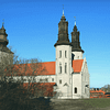 A photograpgh of Sankta Maria cathedral taken from a distance. The church is white with dark colored spires. The sky is very blue.