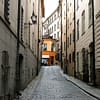 A photo of a Stockholm Old town alley. The alley is dark and dreary, with the sun and a colorful building visible at the very end of it.