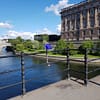 A photo of the Riksbron bridge in Stockholm. There is an imposing stone building to the right, water below, and a blue summer sky above.