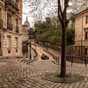 A photo of a cosy cobblestone street in Montmartre in Paris. Little stone houses are lining the street on both sides.