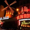 A night time photo of the Moulin Rouge in Paris, the bright neon signs illuminating the dark street.