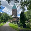 A photo of Old Aker church in Oslo. The sandstone church is in the middle of the lush, green cemetery.