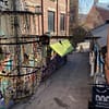 A photo taken from above Ingensteds alley in Oslo. Old factory buildings covered in graffiti have been turned into a market area. A glass chandeleir is hanging in the middle of the alley.