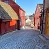 A photo of the old wooden houses at Damstredet in Oslo. Red houses are crowded along a narrow cobblestone street.