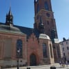 A photo of the Riddarholmen church in Stockholm. The church is a large, gothic, red brick building with green copper towers.