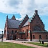 Ett foto av St Nicolai kyrka i Trelleborg. Kyrkan är i rött tegel, med trappgavlar. det är en fin sommardag med blå himmel och stackmoln.