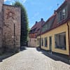 A photo of a Visby street. An old stone wall is visible to the right, and a low, yellow mortared building to the left of a narrow cobblestone street.