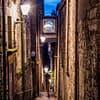 A narrow alley is lit up by a lantern attached to the wall. Steep steps descend into darkness
