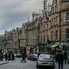 A photo of Cockburn street in Edinburgh on a grey day. People are rushing across a busy street.