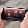 A close up photo of hand holding a smartphone. on the screen is an illustration of a haunted house with ghosts in the windows.
