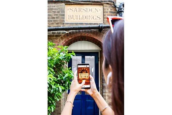 A woman is holding up her smartphone against a brick facade with a signs that says Sarsden building