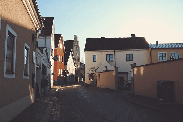 A photo of Strandgatan in Visby. There is a cobblestone street with low white, pink and yellow stone buildings lining it.