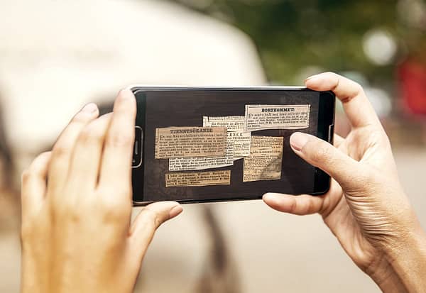 A closeup of a mobile phone screen. on screen are several old newspaper articles visible