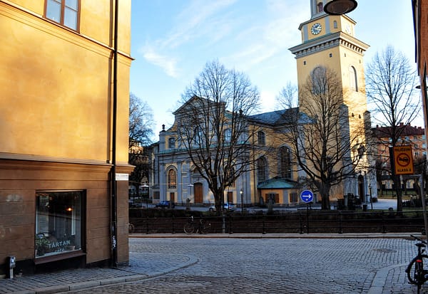 A sunset view of the Maria Magdalena church in Stockholm. It is a yellow stone building with a large belltower with green details.