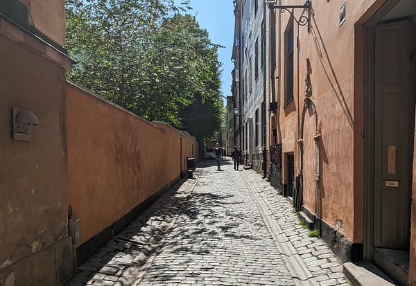 A narrow alley in Stockholm old town. The alley is paved with cobblestones and the buildings on either side are a pale yellow.